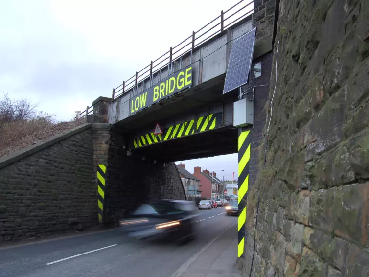 Car driving under low railway bridge with hi-vis markers.