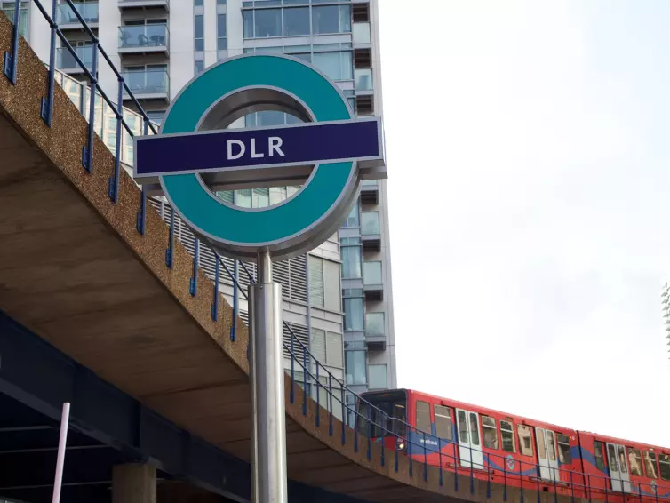 Letrero del DLR con un tren al fondo.