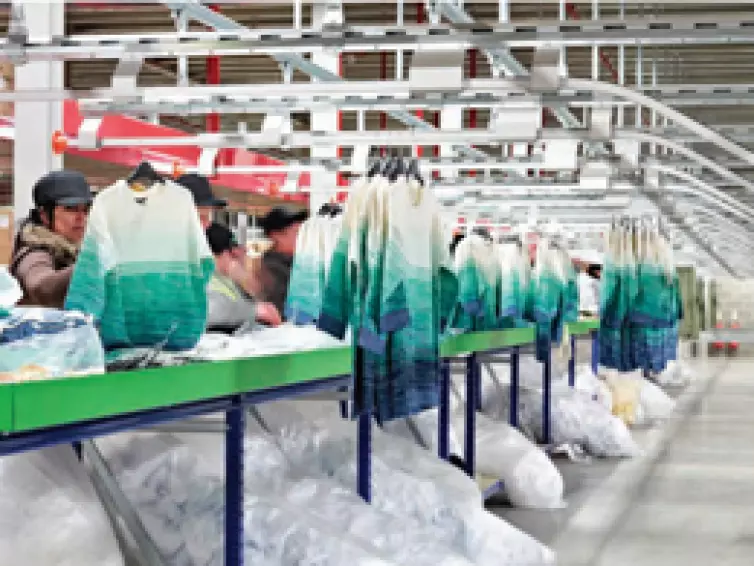 People packing clothes on production line with hanging conveyor system.