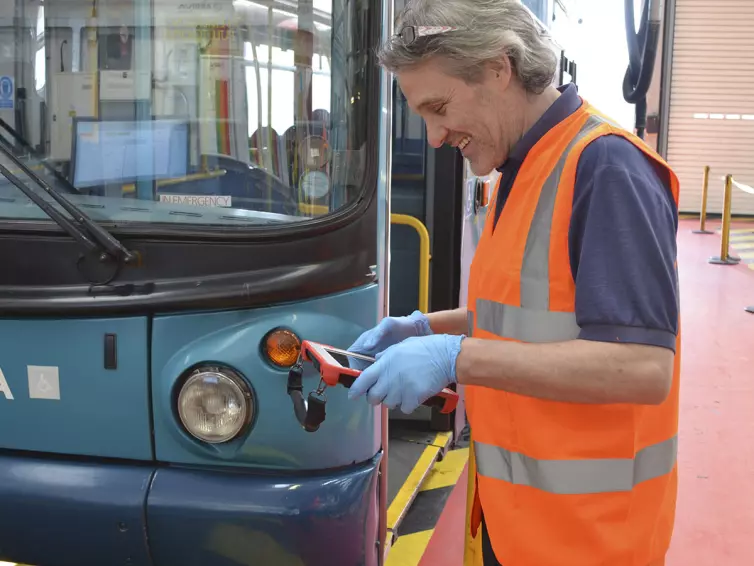 homme utilisant une tablette à côté d’un bus.
