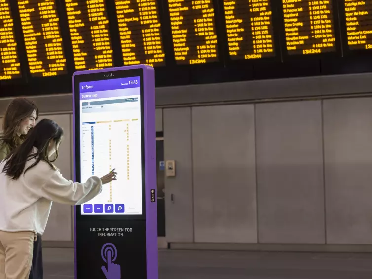 2 girls using inform digital totem at London train station.