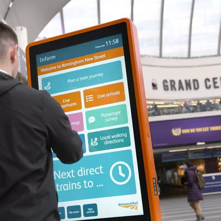 Mann mit Touchscreen-Informationstotem in einem Bahnhof.