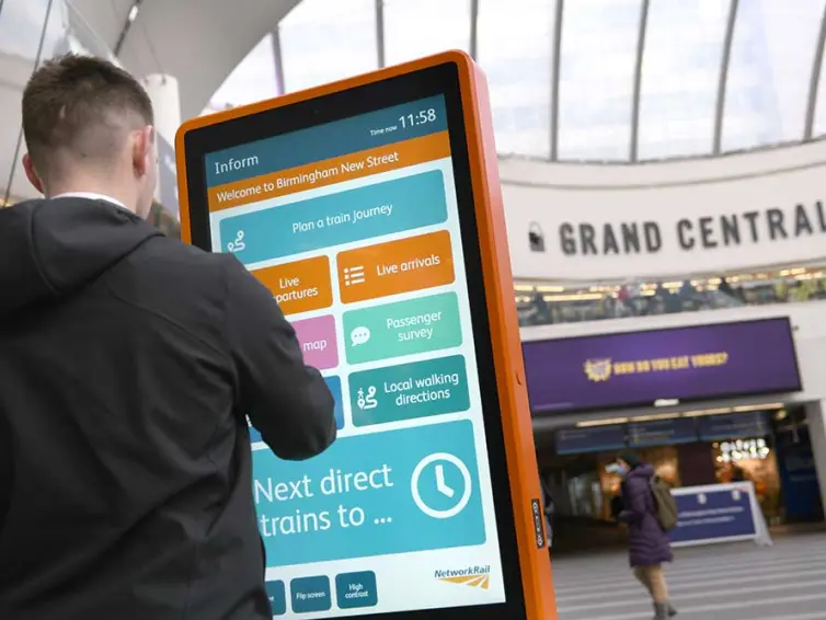 Mann mit Touchscreen-Informationstotem in einem Bahnhof.