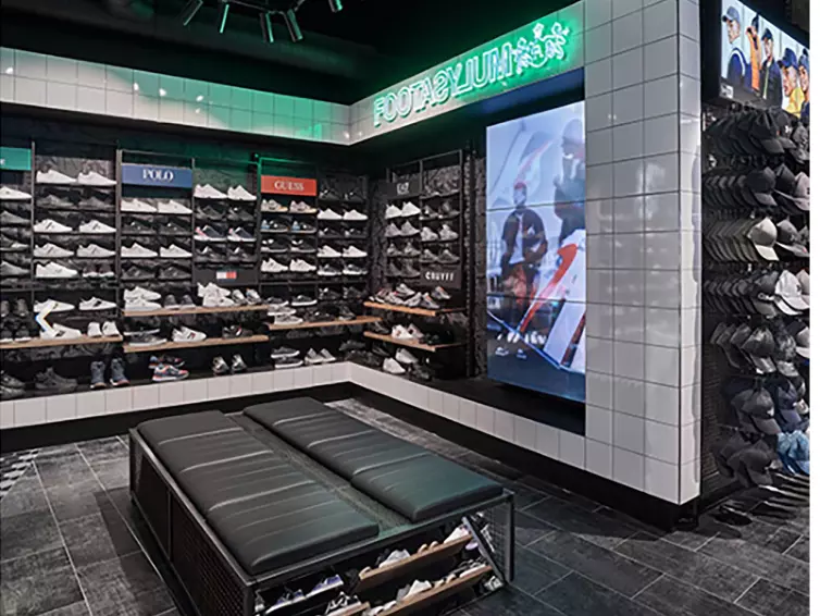 Trainers on shelves inside Foot Asylum shop with digital screen.
