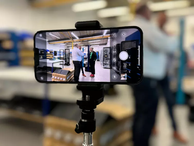 an image of a phone taking a picture of David Clarke, Dagan Bradbury, and Lilian Greenwood at L.B. Foster's Nottingham site.