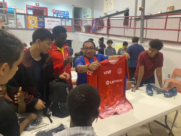 grupo de meninos recebendo camisetas vermelhas com a marca L.B. Foster.