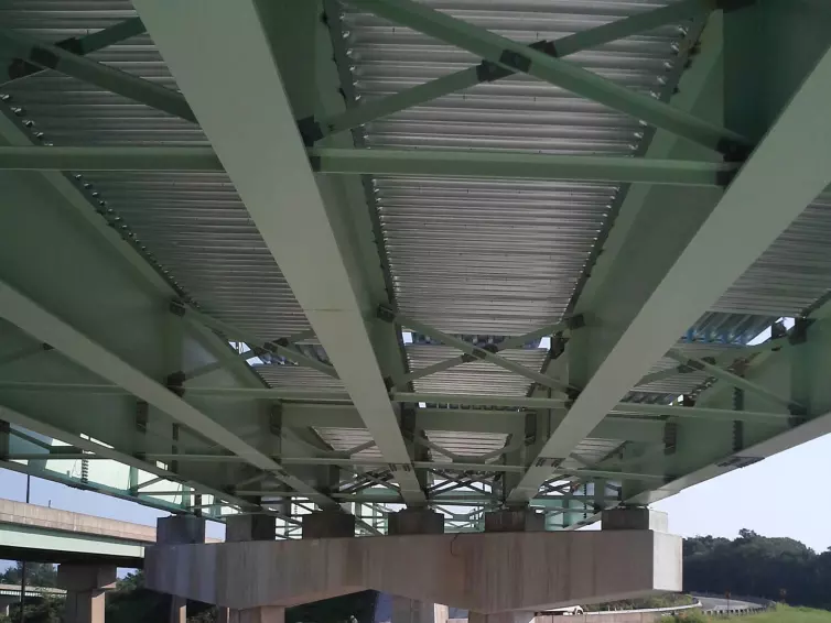 steel bridge decking shown from underneath a bridge with green beams.