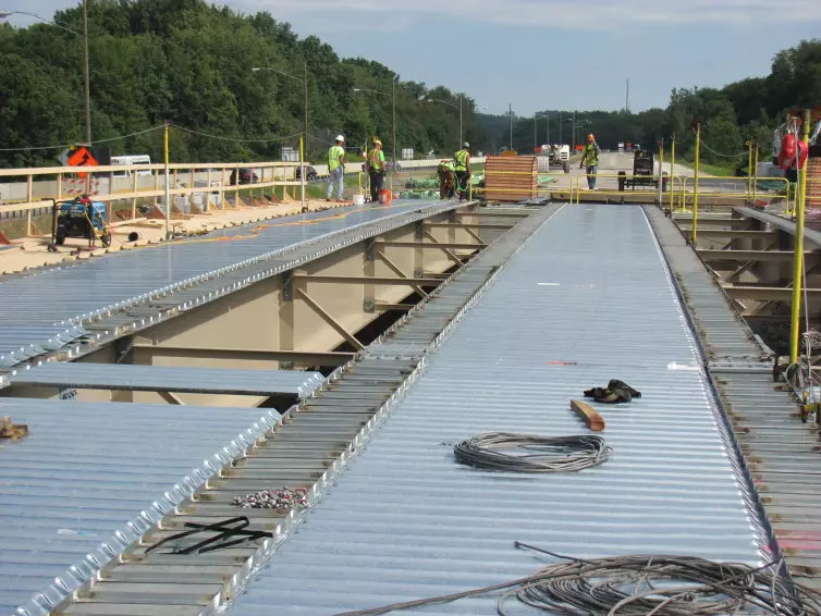 two rows of steel bridge decking placed on a bridge construction site with workers in the background.