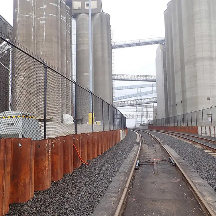 Industrial rail tracks running through grain elevator complex with monitoring equipment for freight car weight detection.