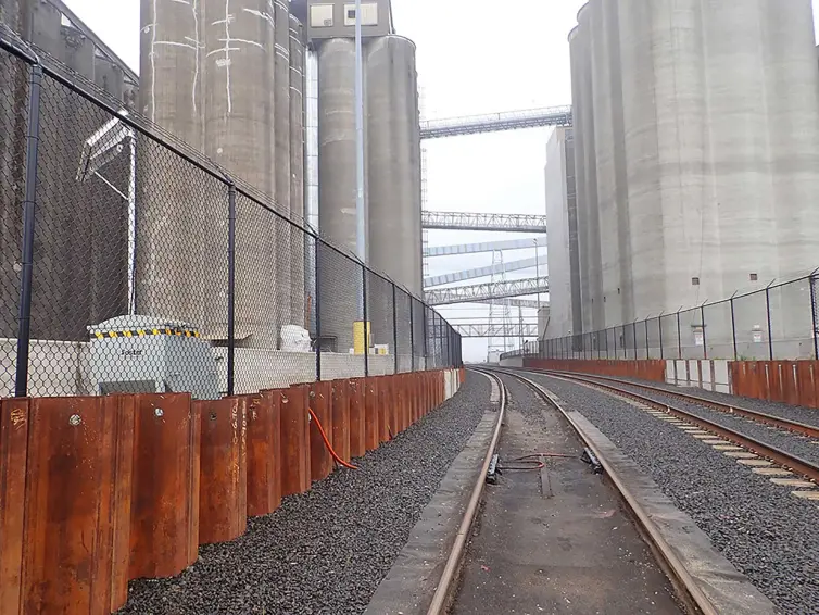 Des voies ferrées industrielles traversant un complexe d’élévateurs à grains avec équipement de surveillance pour la détection du poids des wagons de marchandises.