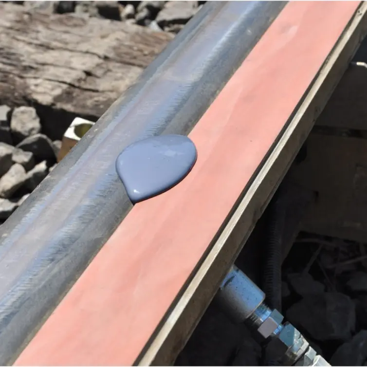 Vue rapprochée d’une voie ferrée où une flaque de liquide gris pourpre est montrée sur une barre de mousse orange fixée au rail.
