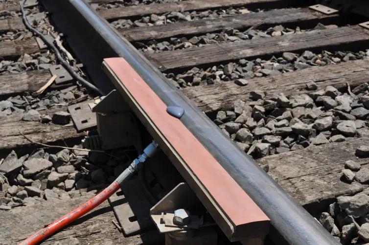 Nahaufnahme eines Eisenbahngleises, auf dem eine Pfütze mit einer violett-grauen Flüssigkeit auf einer orangefarbenen Schaumstoffstange zu sehen ist, die an der Schiene befestigt ist.