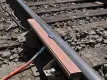 Nahaufnahme eines Eisenbahngleises, auf dem eine Pfütze mit einer violett-grauen Flüssigkeit auf einer orangefarbenen Schaumstoffstange zu sehen ist, die an der Schiene befestigt ist