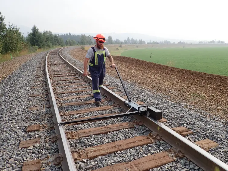 Homem andando em um trilho de trem com um dispositivo no trilho para testar o desempenho.