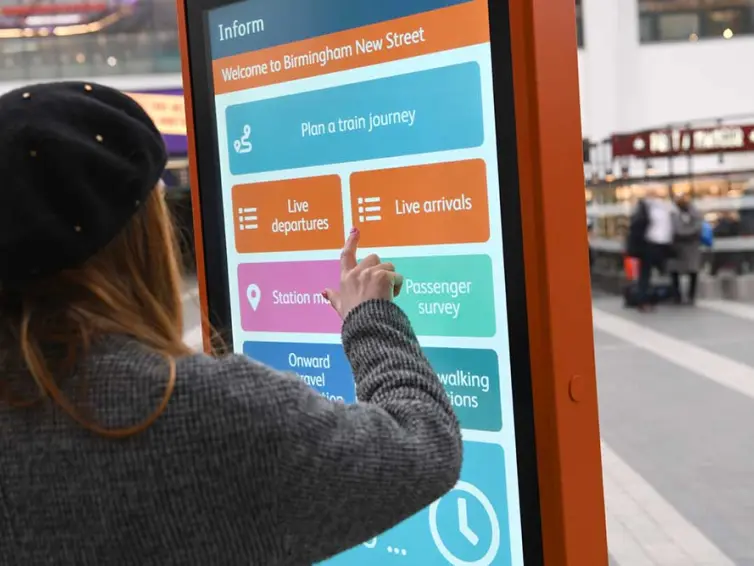 Frau mit Touchscreen-Totem im Bahnhof.