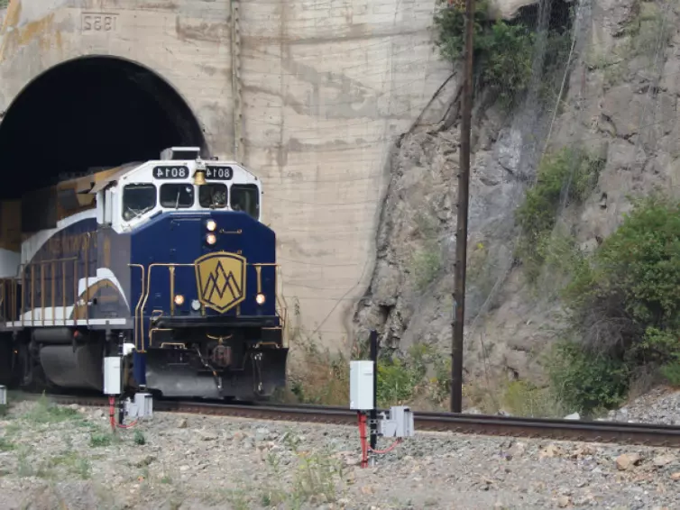 Ein Zug fährt durch einen dunklen Tunnel, wobei der Kontrast zwischen dem beleuchteten Zug und der schattigen Passage hervorgehoben wird.