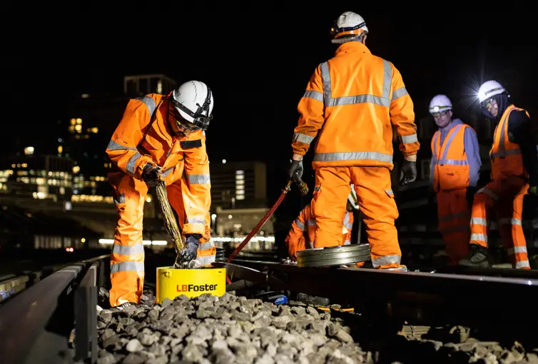 Operários com equipamento de proteção trabalhando em trilhos de trem.