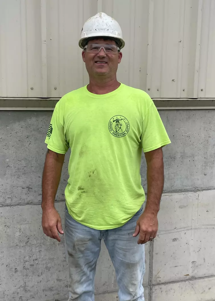 Homme souriant portant une chemise vert vif haute visibilité, un casque de sécurité blanc et des lunettes de sécurité.