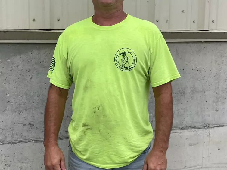 Man smiling wearing a high-vis bright green shirt, a white hard hat, and safety glasses.