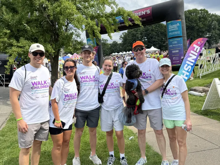 Family smiling and holding a dog. (L-R) Mark, Bella, Alex, Heather, Jack the family dog, Bill Thalman, Executive VP & COO, and Diane.
